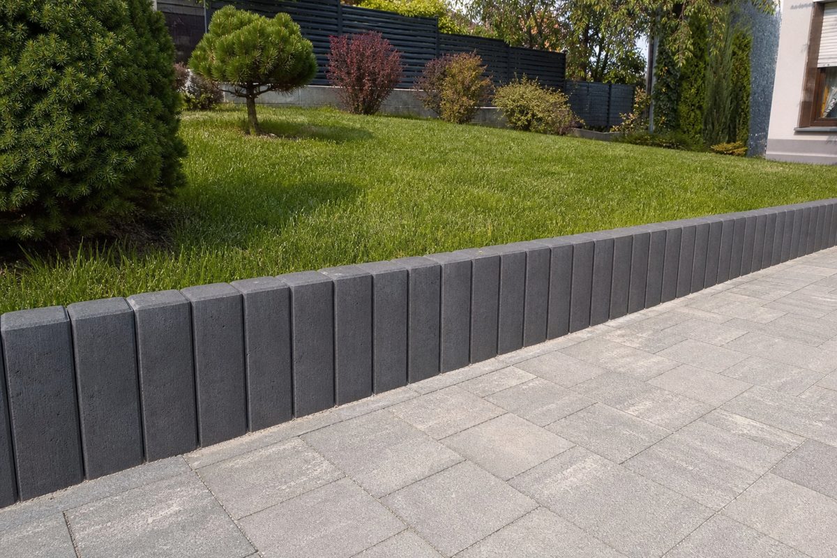 Palisady betonowe w kolorze grafitowym jako obrzeże trawnika przy ścieżce z kostki
